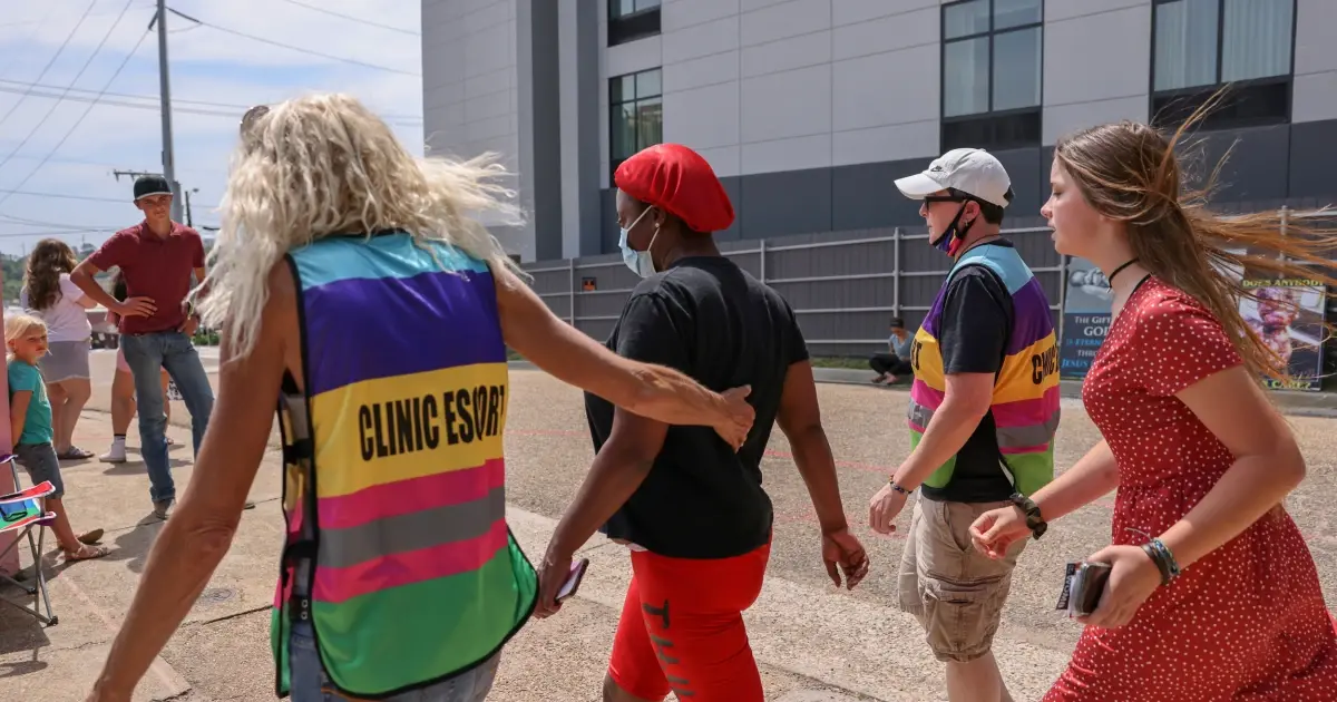 A photo of volunteers in clinic escort vests walking with a person outside a clinic.